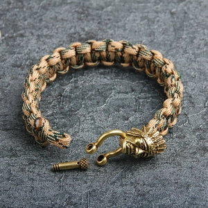 Paracord survival bracelet with brass Indian chief buckle on a rugged stone surface