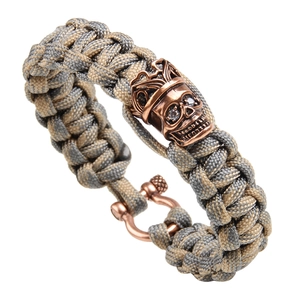 Paracord survival bracelet with crown skull bead and bronze U-shackle clasp on white background