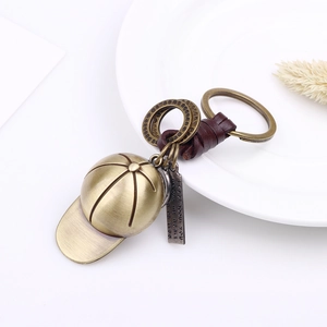 Vintage bronze baseball cap keychain with brown leather cord on a white ceramic plate
