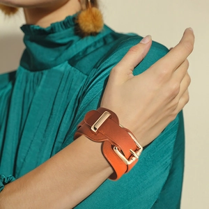 Wide orange faux leather cuff bracelet with gold buckle shown on a female wrist