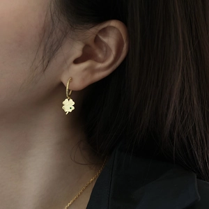 Close-up of a gold clover earring with a green gemstone on a model with black hair