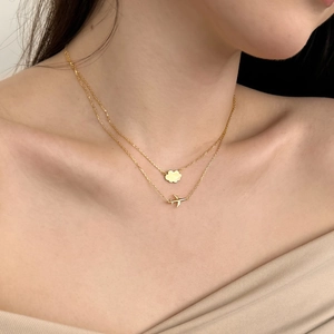 Detailed close-up of double-layered gold necklace with plane and cloud pendants