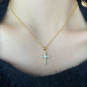 Detail of a gold cross pendant necklace with zircon inlay on a model's neck