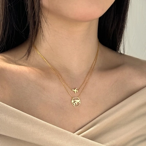 Close-up of gold double-layer necklace featuring airplane and world map pendants