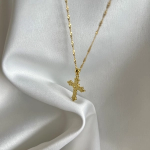 Macro detail of a golden cross pendant with zircon inlay on a white silk surface