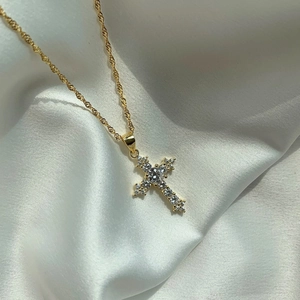 Detail of gold cross pendant with sparkling zircons on white silk fabric background