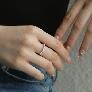 Detailed view of a rose gold pavé ring with round zircons worn on a model's hand