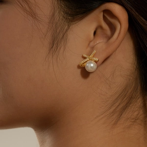 Elegant gold bow earrings with shimmering zircon and round white pearl on female model