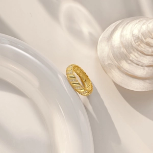 Close-up of a twisted 18k gold-plated silver ring with zircon inlays on a white ceramic tray