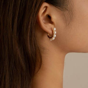 Close-up of elegant gold hoop earrings with freshwater pearls on a model's ear
