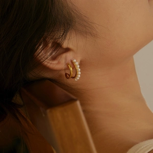 Close-up of golden S925 silver double hoop earrings with white pearls on model ear