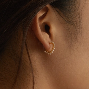 Elegant heart-shaped gold earrings with pearl border detail worn on ear
