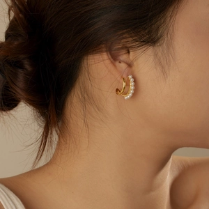 Elegant gold double-hoop earrings featuring white pearls worn on a model's ear
