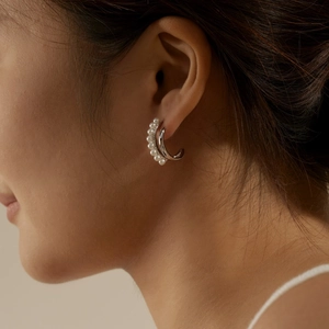 Close-up of double C-shaped silver earrings with small white pearls on a female ear