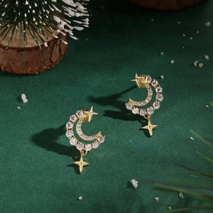 Gros plan des boucles d'oreilles lune et étoile dorées sur fond de Noël vert élégant