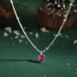 Detail der S925 Silberkette mit herzförmigem rosa Edelstein auf festlichem Hintergrund