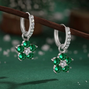 Détail de boucles d'oreilles fleur en argent avec cristaux verts sur branches enneigées