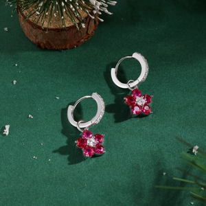 Détail de boucles d'oreilles fleur en argent S925 et gemmes rouges sur fond festif