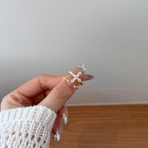 Dettaglio di un anello a croce dorato regolabile con zirconi brillanti sulla mano