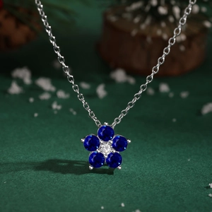 Détail macro du collier en argent S925 avec pendentif fleur en gemme bleue sur fond vert foncé