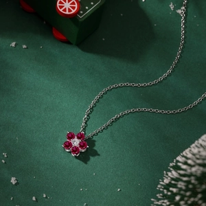 Vue macro d'un collier fleur en argent avec pétales en pierres rouges sur fond de Noël