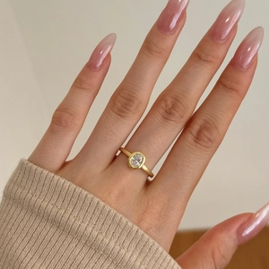 Detail of oval-cut zircon ring with matte gold band on model's hand with warm knitwear