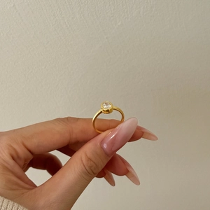 Close-up of gold plated ring with matte texture and bezel-set round brilliant zircon