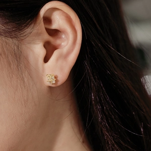 Close-up of golden gift box stud earrings with crystals and bow detail on ear