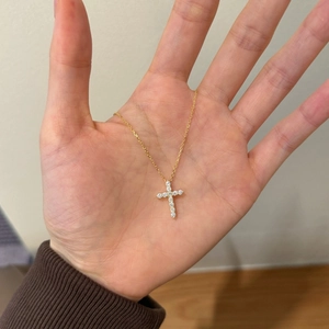 Detailed view of hand holding a gold S925 silver cross necklace with sparkling zircon stones