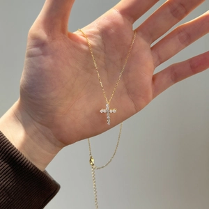 Detailed view of a gold cross pendant necklace featuring sparkling zircon inlay on hand