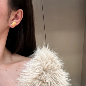 Detailed close-up of a brushed gold butterfly earring with white crystals on a model