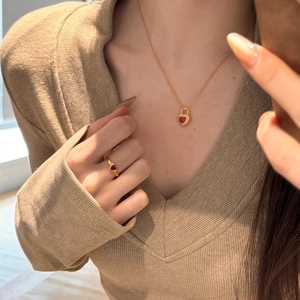 Detail of heart-shaped gold necklace and ring set with red zircon on a model