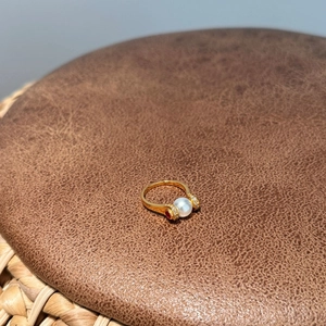 Detail shot of golden ring with 8mm pearl, zircons, and red ruby accents on leather