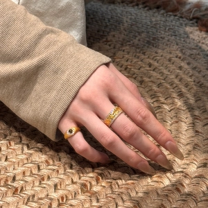 Detail of vintage gold textured ring with leaf patterns and green gemstone on model hand