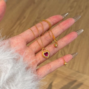 Detail of a gold heart necklace with red gemstone and white crystal halo on a gold chain