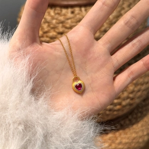 Close-up of heart-shaped ruby pendant necklace with gold chain worn on female hand