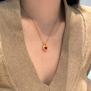 Close-up of a gold heart-shaped ruby pendant necklace worn with a beige knitted sweater