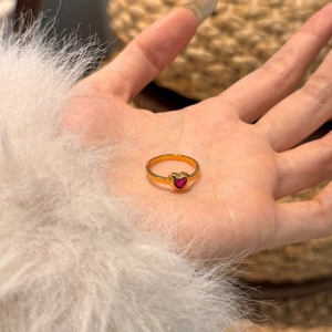 Macro shot of an elegant gold heart ring with red gemstone held in palm on soft texture