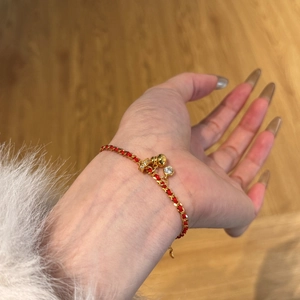 Detail of red woven bracelet featuring a gold bell and a crystal charm on a woman's wrist