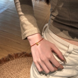 Detail of a red braided rope bracelet featuring a gold heart charm and zircon on a wrist