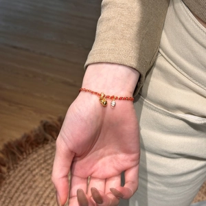 Close-up of red braided rope bracelet with golden bell and zircon pendant on wrist