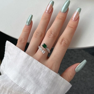 Close-up of emerald-cut green gemstone ring with pavé diamonds on silver adjustable band