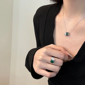 Détail d'un ensemble collier et bague en émeraude porté sur un vêtement noir en tricot