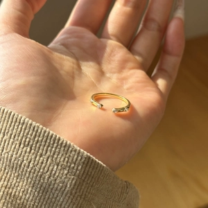 Close-up of minimalist gold open ring with round clear stones held in hand