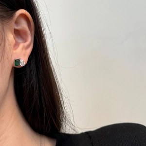 Gros plan de boucles d'oreilles asymétriques avec gemme verte émeraude et pierre blanche