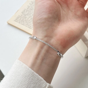 Eleganter S925 Silberarmreif mit Tropfensteinen am Handgelenk vor einem Buch
