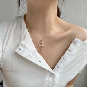 Dettaglio di una collana a croce dorata con perle e cristalli indossata sul collo