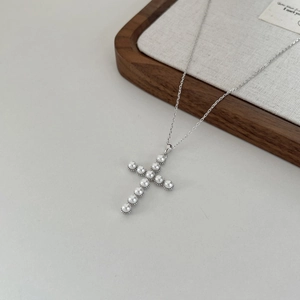 Detail of cross pendant with inlaid pearls and silver metal chain on a minimal background