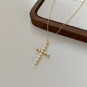 Close-up of golden cross pendant featuring round white pearls on a matching fine chain