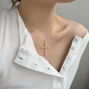 Elegante collana a croce dorata con perle e zirconi indossata con uno stile vintage
